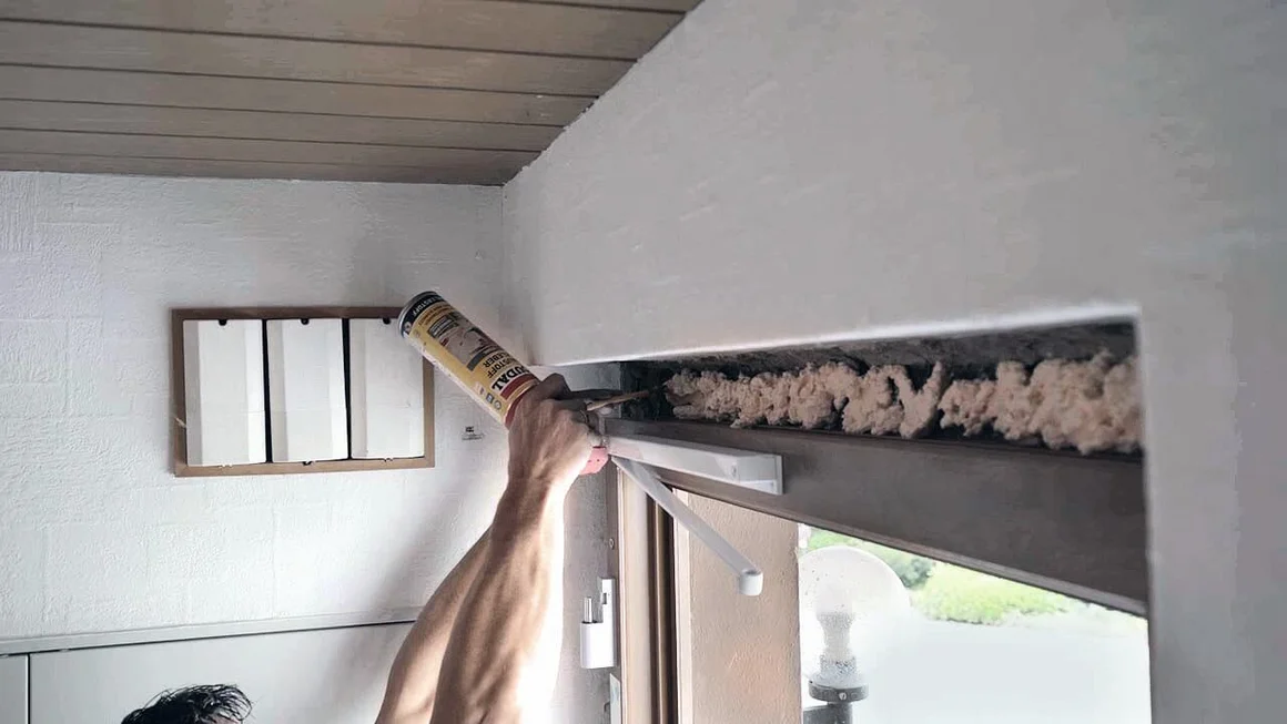 Person dichtet Türrahmen mit Schaumstoff ab.